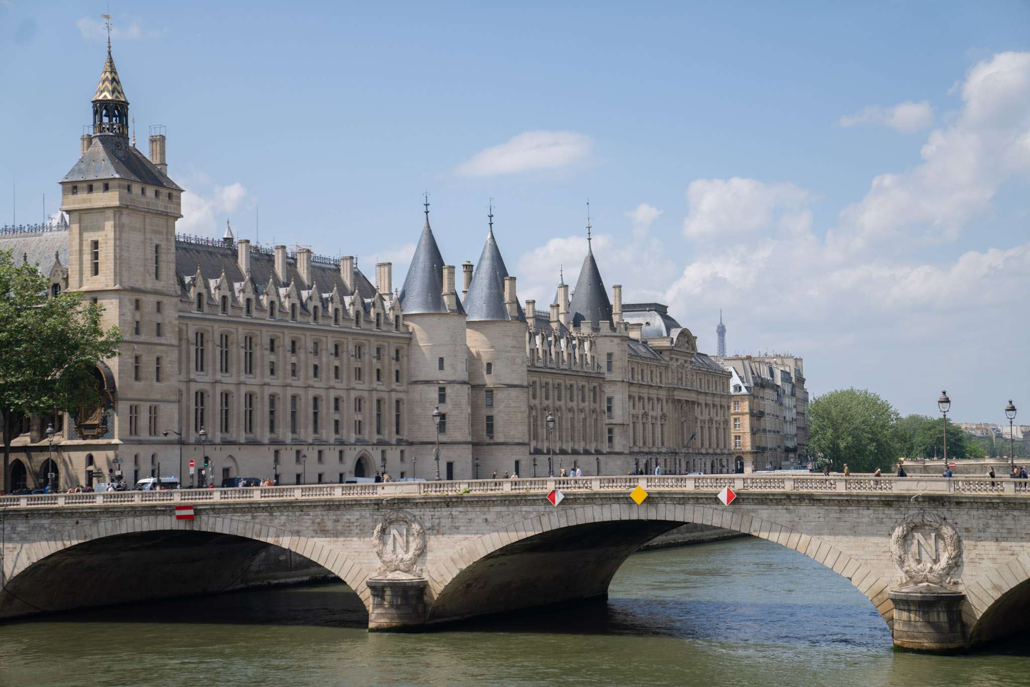 Photo prise depuis les quais de Seine, montrant le Pont au Change avec des piétons et des véhicules. À gauche, le Palais de Justice est visible. La photo est prise en pleine journée.