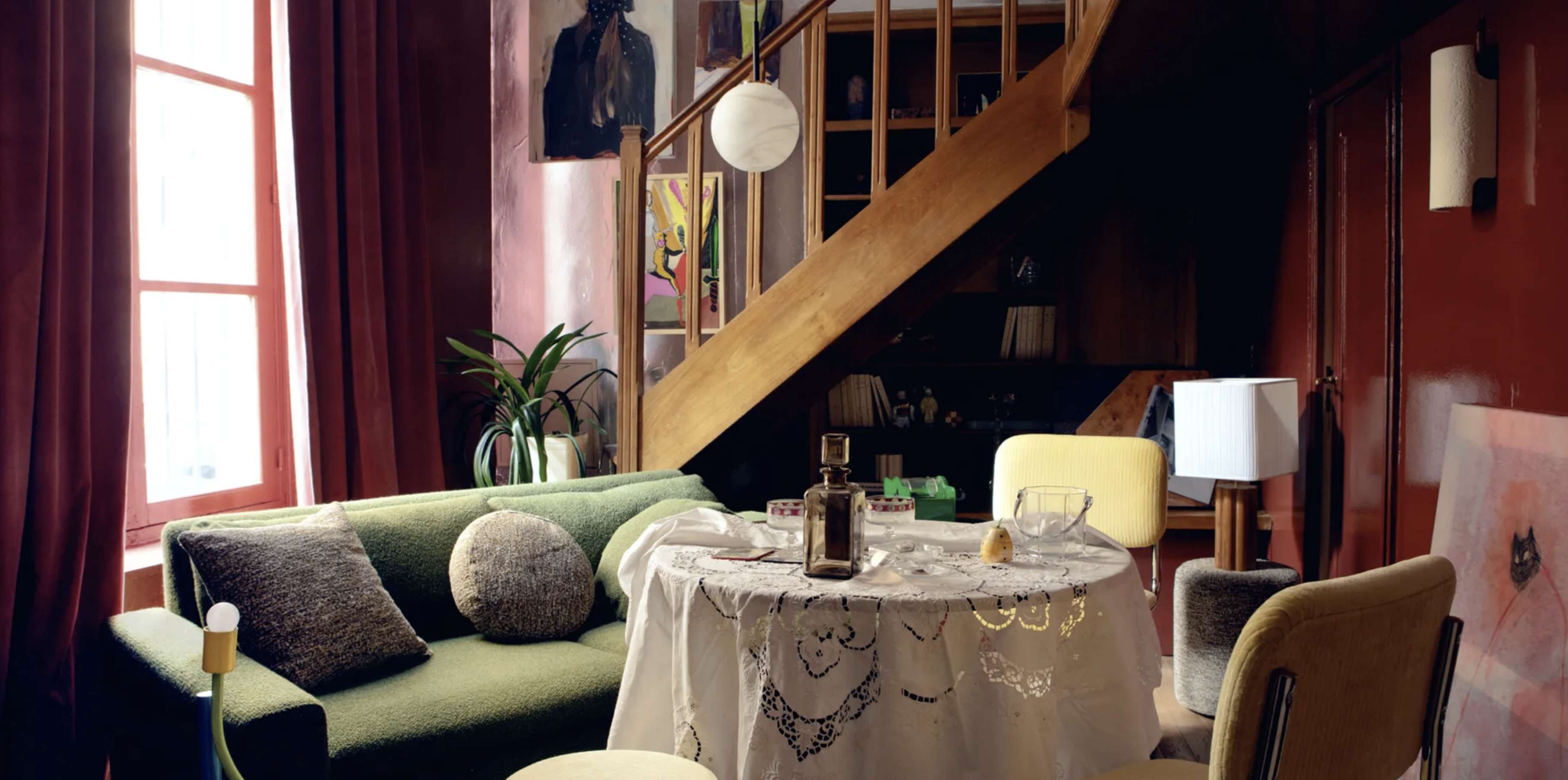 Ambiance feutrée pour cette salle à manger avec une table recouverte d'une nappe en dentelle blanche, un canapé et des fauteuils verts et des murs sang de boeuf