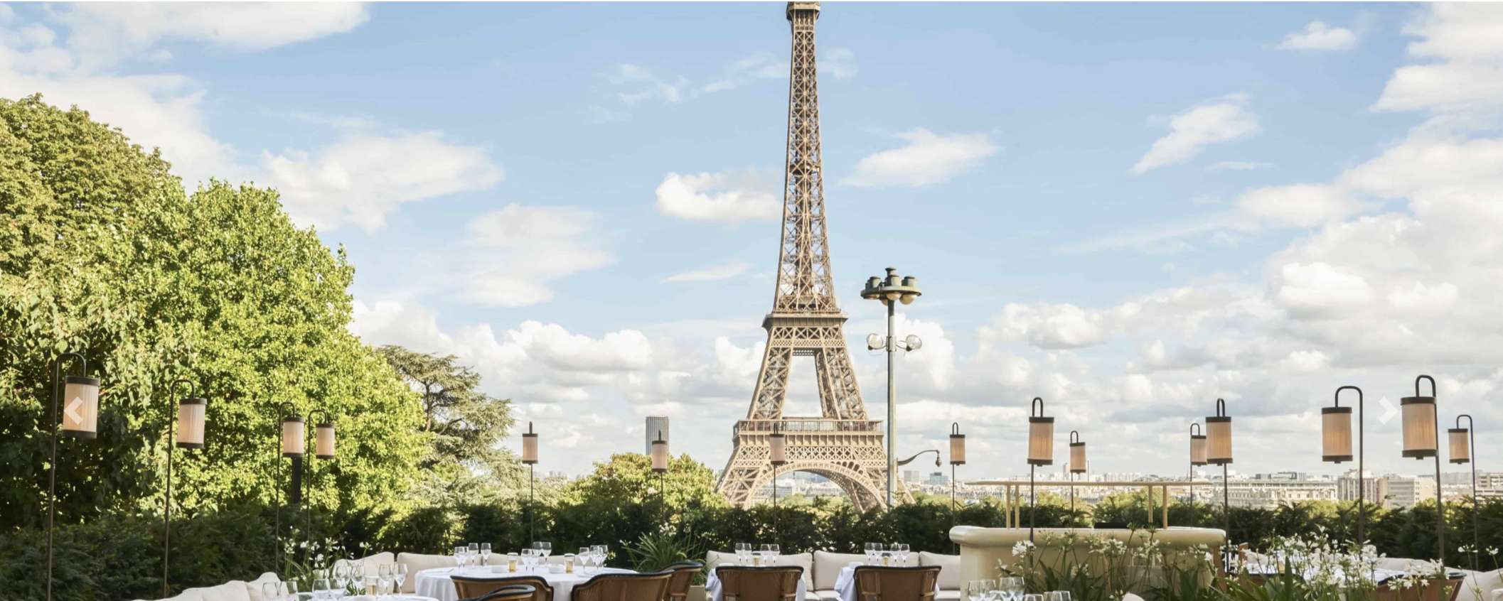 Terrasse d'un restaurant à Paris avec des tables dressées et des couverts. En arrière-plan, on aperçoit la Tour Eiffel.