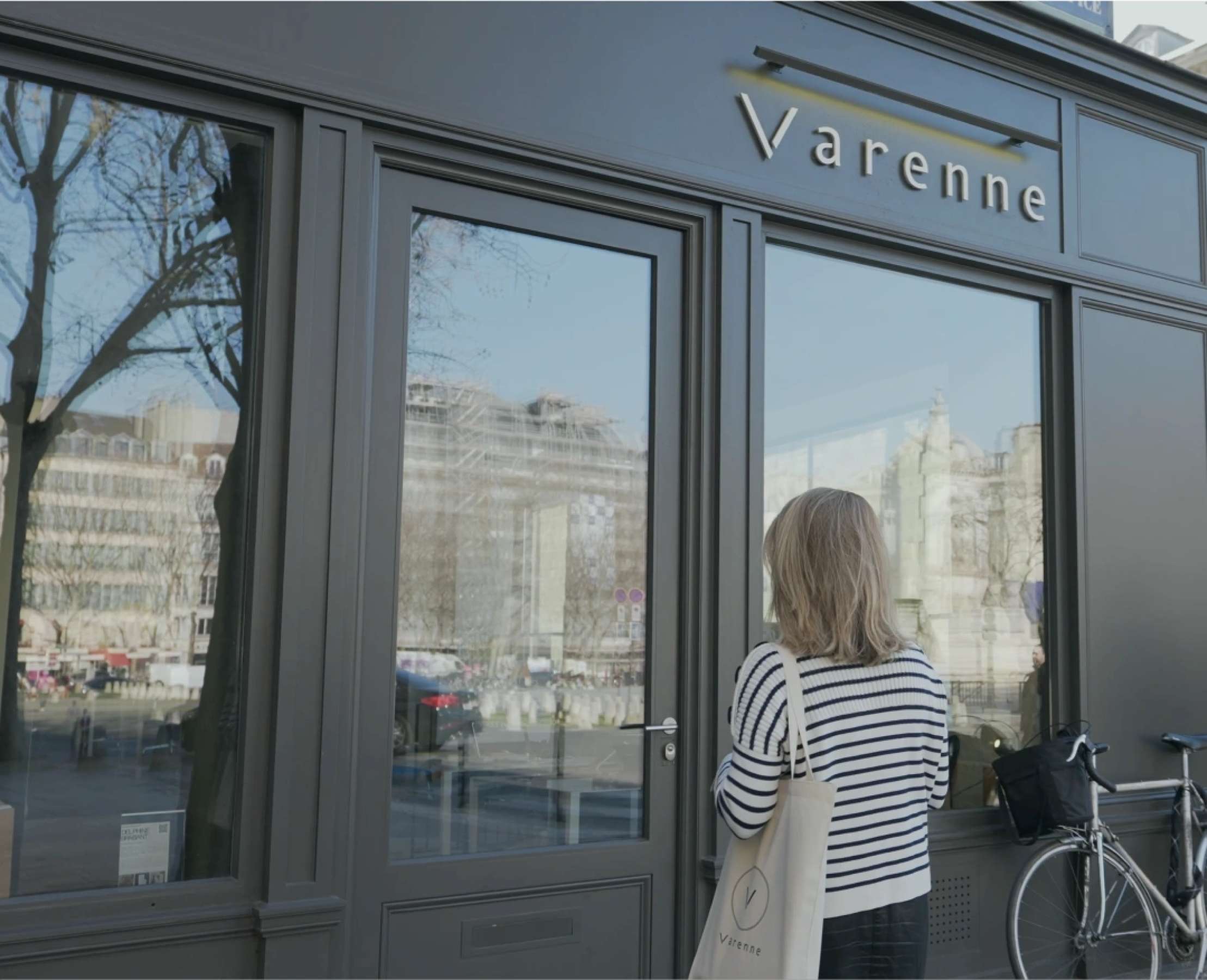 Façade vitrine de l'agence Varenne avec une grande vitrine, une personne de dos en train d'entrer, habillée d'une marinière